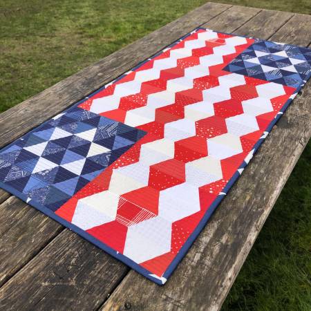 This table runner is the perfect choice for the summer holidays. Construction is simple – there are no Y seams. Since the design is created with a combination of triangles, trapezoids and half-triangles, it is a great way to learn how to use the ruler. The star field on opposite corners makes the finished project read “right side up” on either side of the table.