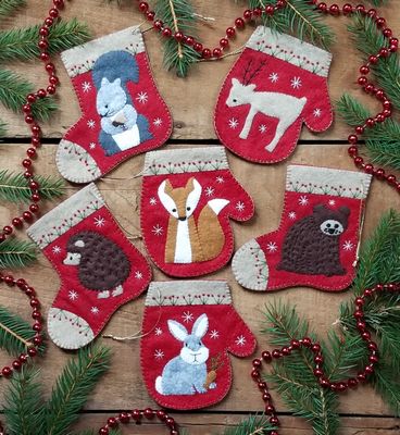 The woodland critters are celebrating Christmas! A pudgy bear, plump bunny, petite deer, prickly hedgehog, pointy fox, and proud squirrel make up this combination of 3 mitten and 3 stocking ornaments. Each ornament is open at the top and can be filled with gift cards or other small treasures. Size is approximately 4 in x 4.5 in. Kit includes woolfelt, embroidery floss and gold string plus precise patterns illustrated instructions to make 6 ornaments. Colors are red, sandstone, brown, gray, white, and amber.