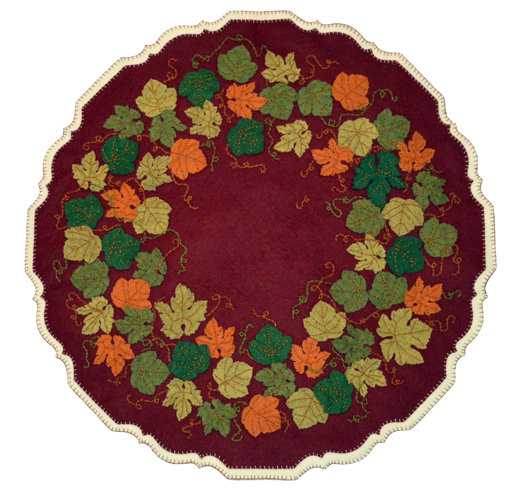 The striking leaf colors against a deep garnet red background evoke memories of crisp fall days. The mat is patterned after the carved edge of a Chippendale style pie crust table typical of the early 1700-1800s. The cream backing accents the edge making it stand out on your table.  This kit makes a 24″ pie crust table cover. The mat uses a back stitch to attach the leaves, a chain stitch for the vines, and a blanket stitch for the edges. It is an advanced kit.