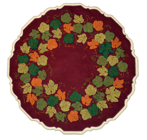 The striking leaf colors against a deep garnet red background evoke memories of crisp fall days. The mat is patterned after the carved edge of a Chippendale style pie crust table typical of the early 1700-1800s. The cream backing accents the edge making it stand out on your table.  This kit makes a 24″ pie crust table cover. The mat uses a back stitch to attach the leaves, a chain stitch for the vines, and a blanket stitch for the edges. It is an advanced kit.